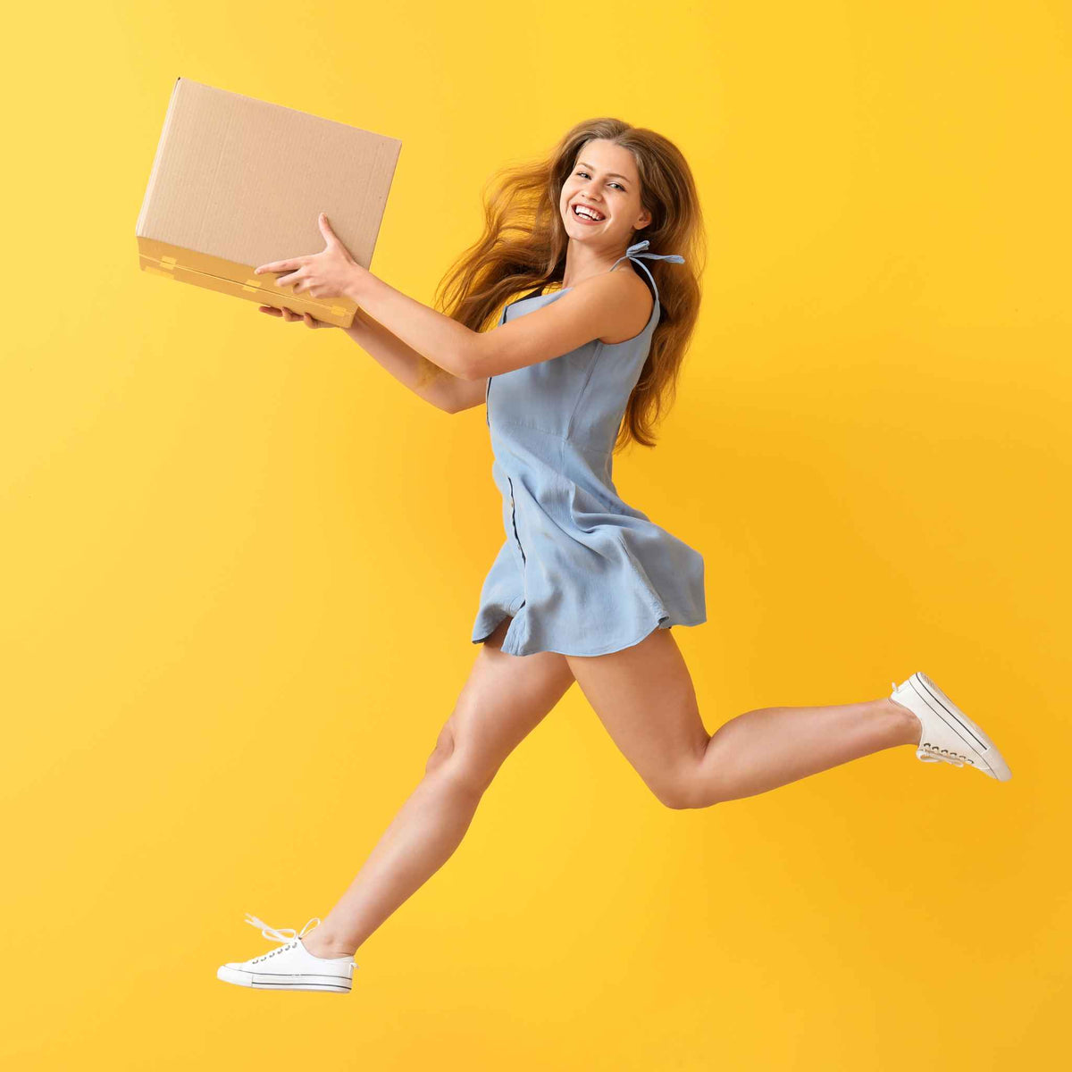 Eine Frau springt und lacht mit einem Paket in der Hand